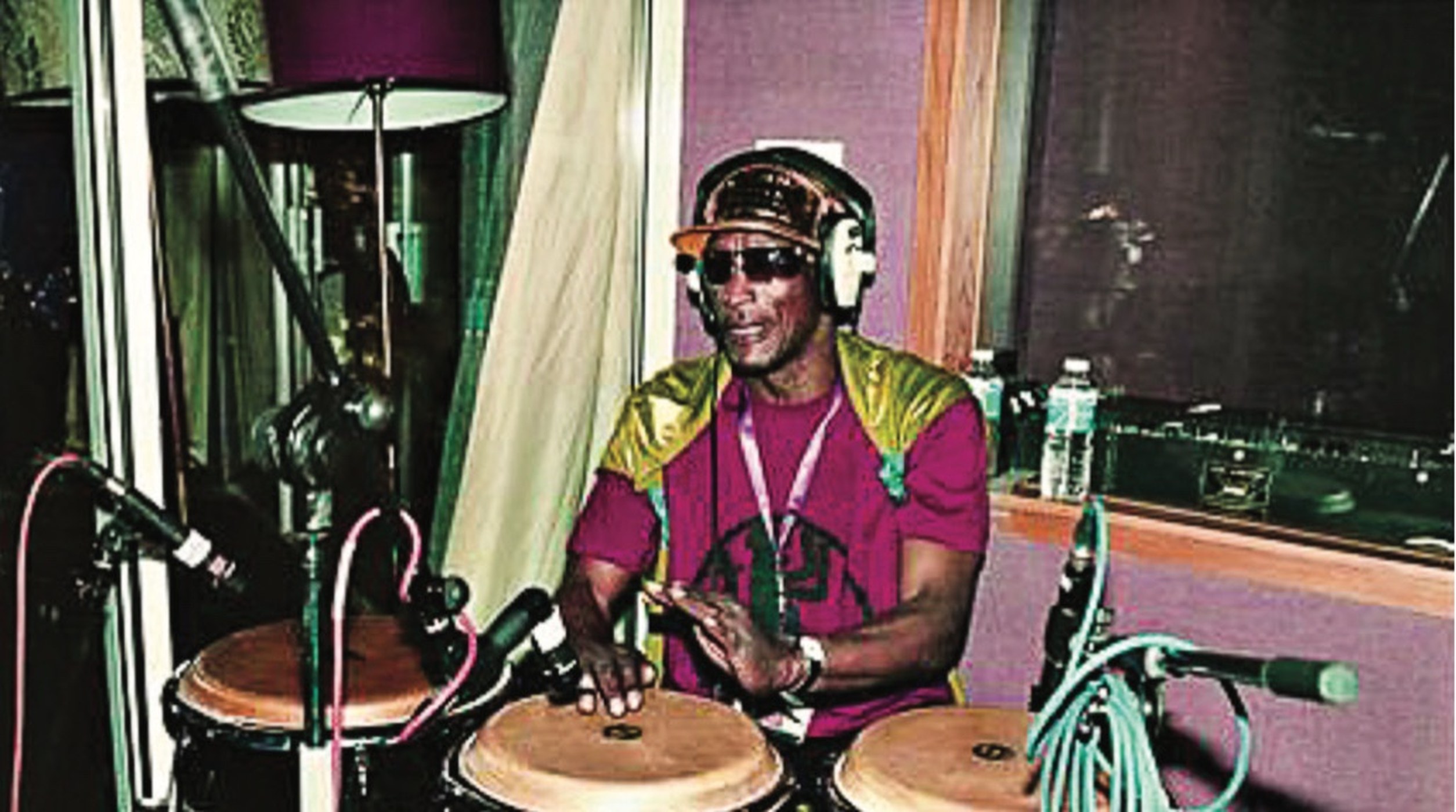 Dad in the studio — cap, shades, headphones on, hands on the congas