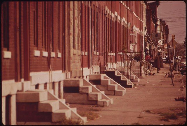 A boy on the sidewalk beside a North Philadelphia rowhouse with flower boxes over the awning, 1973