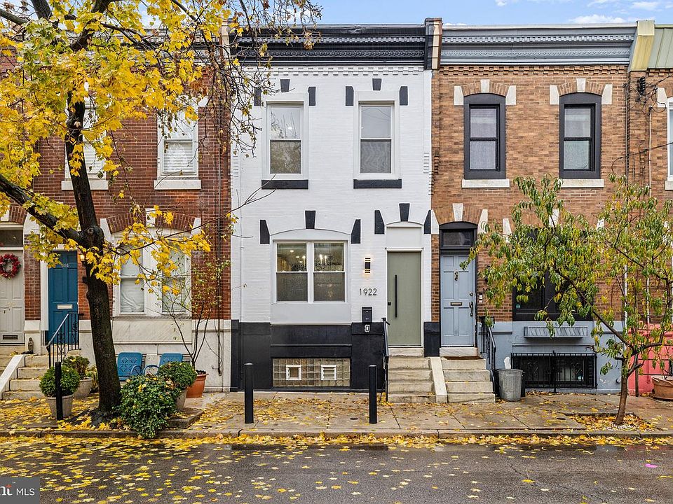 North Philadelphia rowhouse with white and black facade between brick neighbors, autumn leaves on the sidewalk